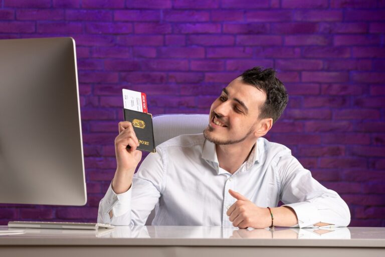"Smiling man holding passport and boarding pass at desk, researching visa and immigration services online"